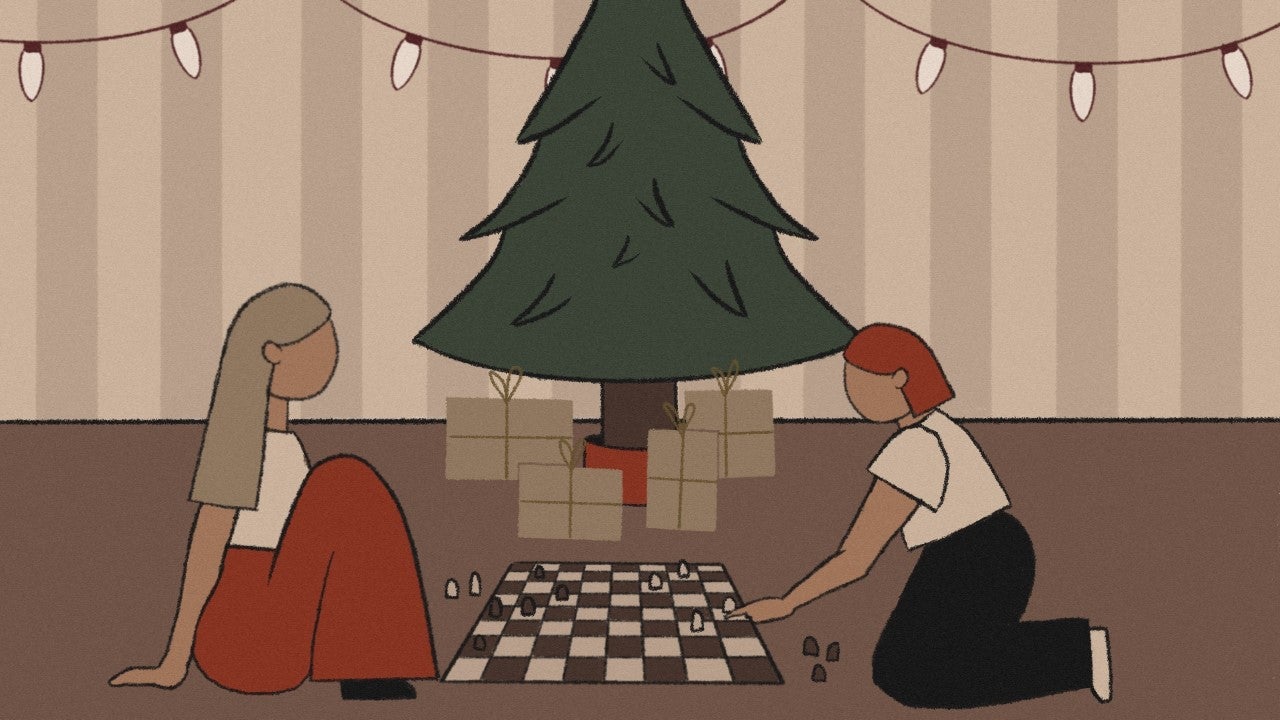 Two people play Chess together in front of a Christmas tree.
