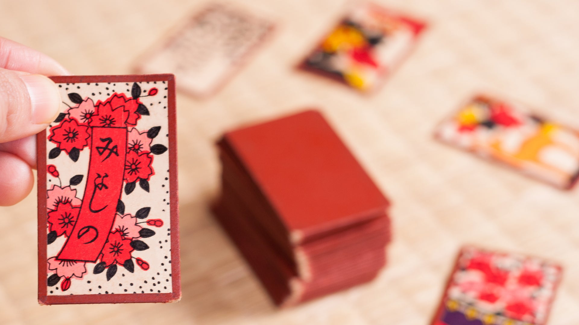 A Hanafuda card held in the foreground with a game being played in the background
