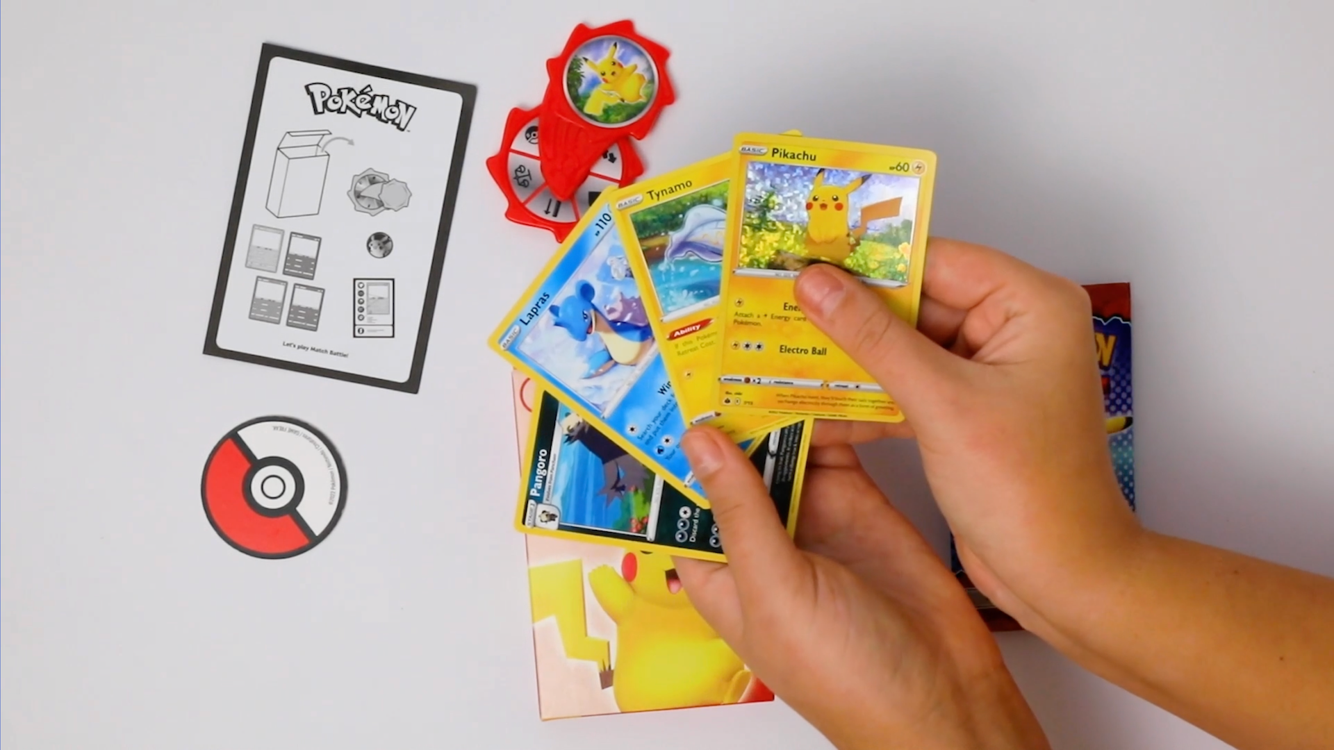 A hand splays out four Pokemon TCG cards found in the newest McDonald's happy meal promotion. On the table is an instruction card, a coin and a plastic spinner.