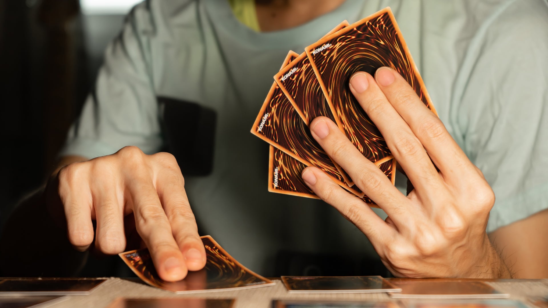 A man holding Yu-Gi-Oh! cards while placing a card on the table